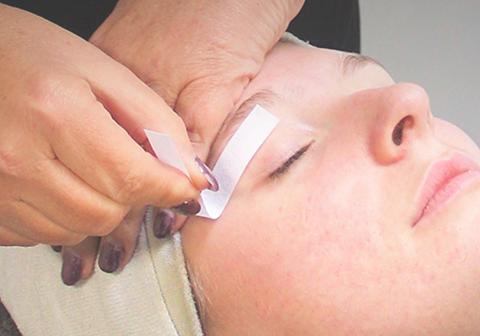 Verzorging en ontspanning in Salon M'iris in Rucphen. Vrouw ligt ontspannen op de behandelingstoel in Salon M'iris, terwijl zij een een hars behandeling krijgt aan haar wenkbrauwen. Verzorging en ontspanning in Salon M'iris in Rucphen.